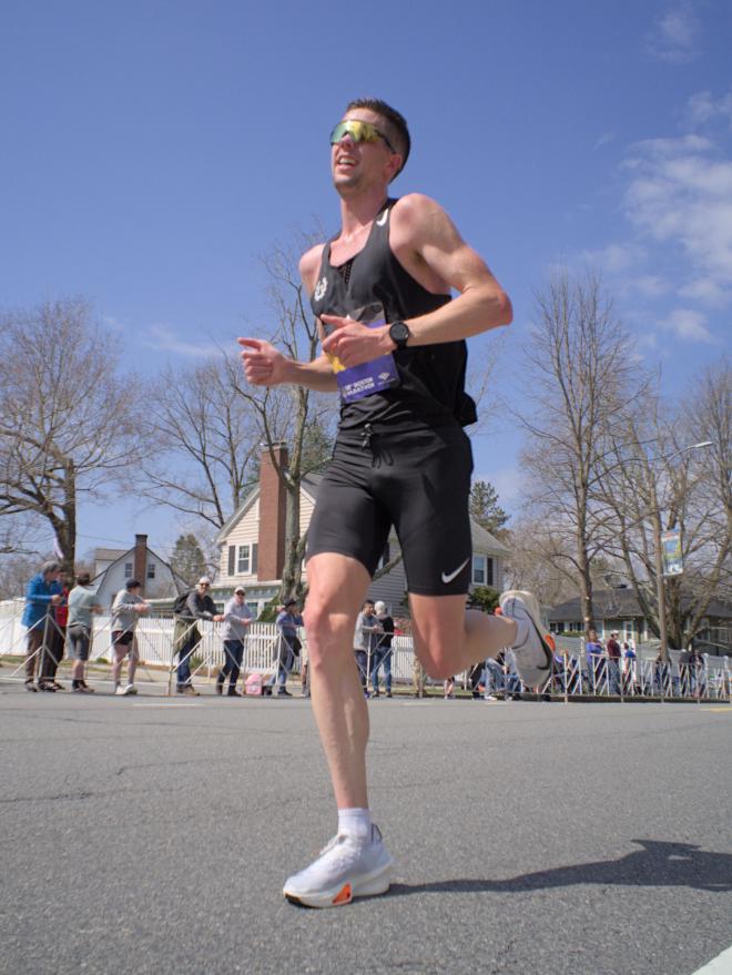 A runner dressed in black with white shoes. He looks very tall, and the low angle of the photo accentuates his height.