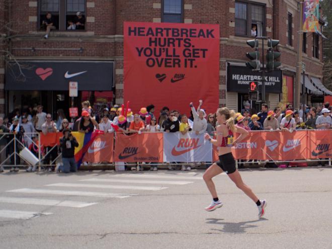 A woman wearing a red and black striped top runs past a sign in matching colors that reads &ldquo;Heartbreak hurts. You&rsquo;ll get over it.&rdquo;