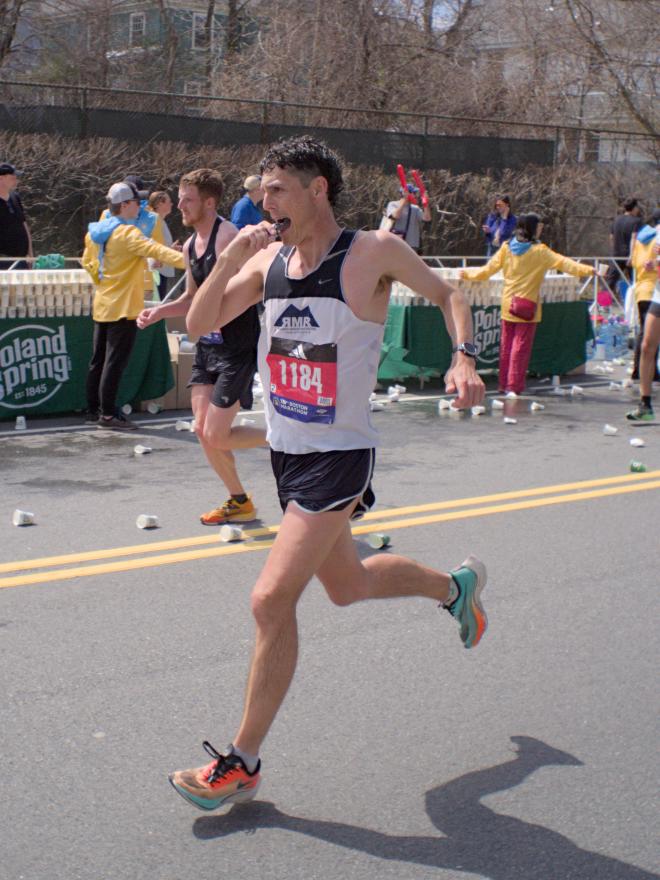 A man mid-bite of a snack as he runs past a water station.