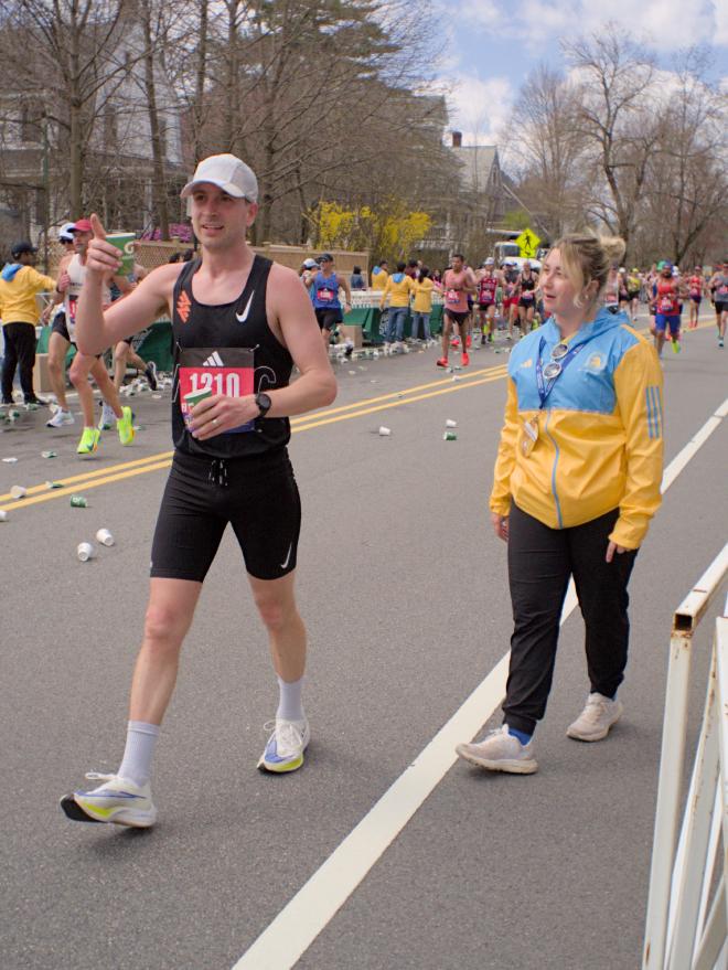 A runner takes a breather at the water station and chats with a member of race staff dressed in a blue and yellow windbreaker.